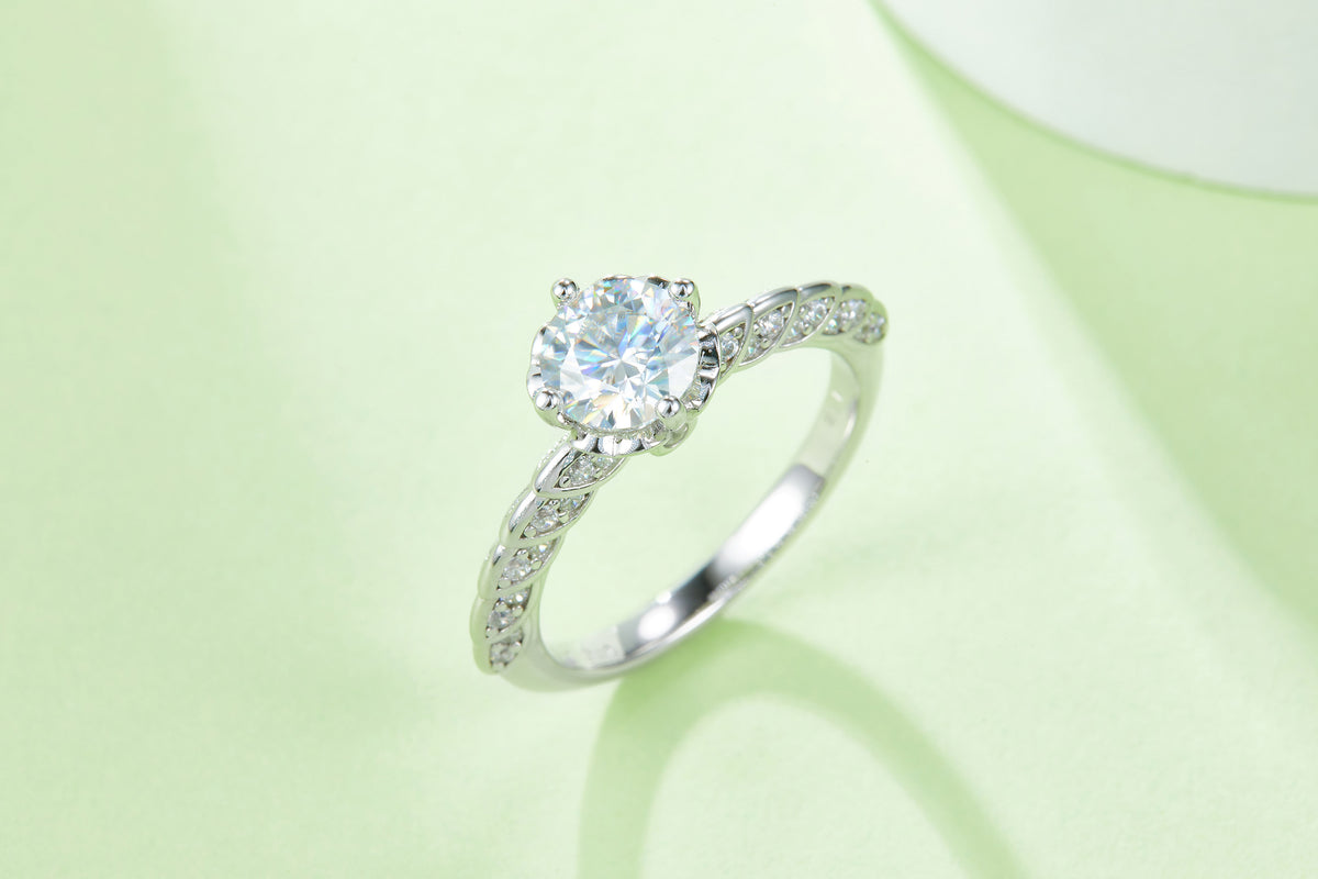 CARISSIE round moissanite solitaire ring, lifestyle shot on a pale green background showcasing the stone's brilliance