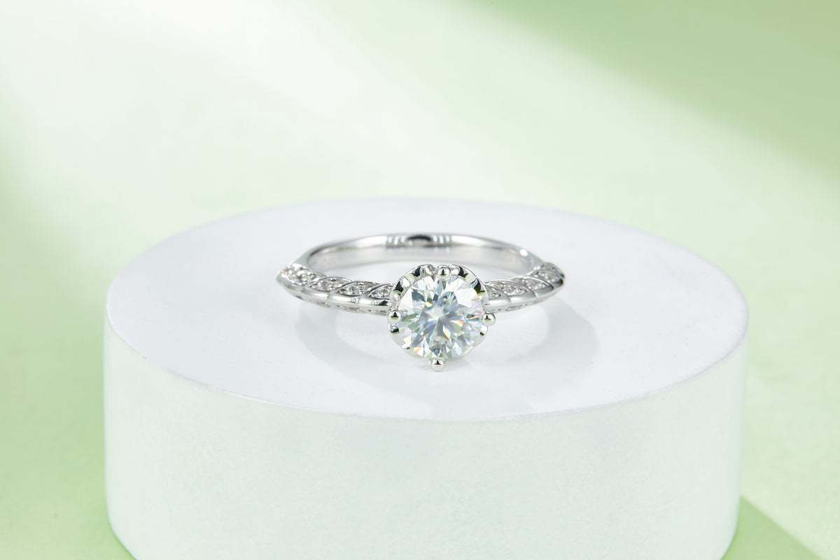 CARISSIE round moissanite solitaire ring, centered view on a white pedestal emphasizing the symmetrical band design