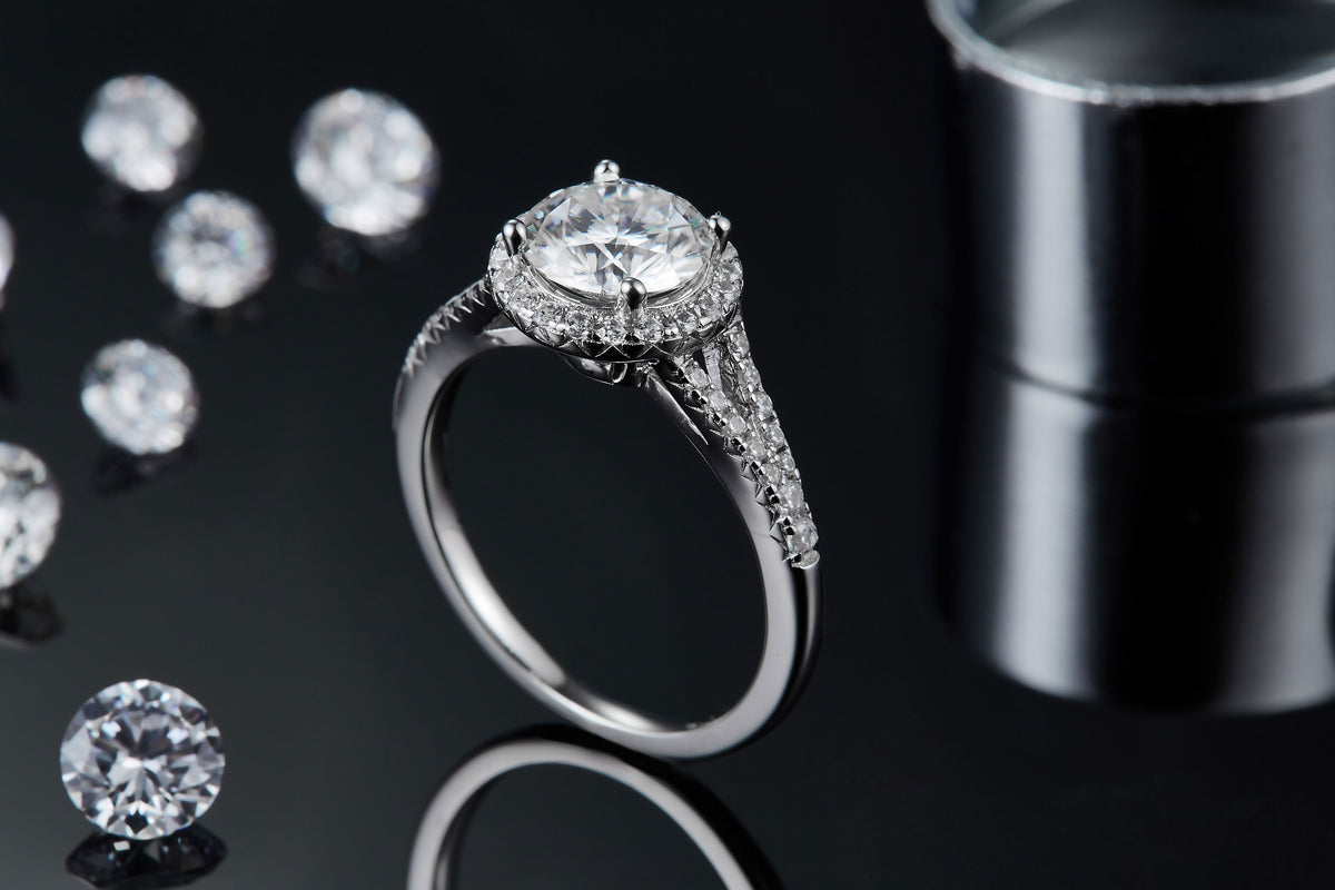 CARISSIE round moissanite halo engagement ring, lifestyle shot on black background with loose stones and reflection