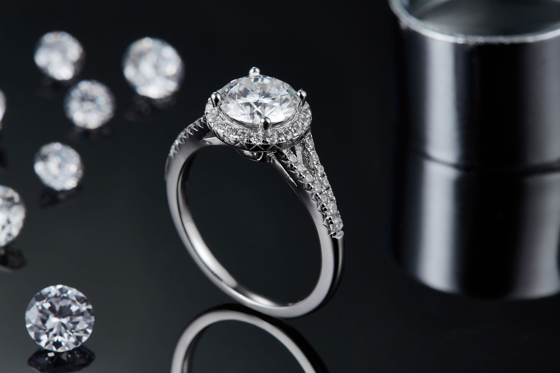 CARISSIE round moissanite halo engagement ring, lifestyle shot on black background with loose stones and reflection