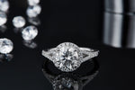 CARISSIE round moissanite halo ring, front view resting on a reflective black surface showing the ring's mirror image