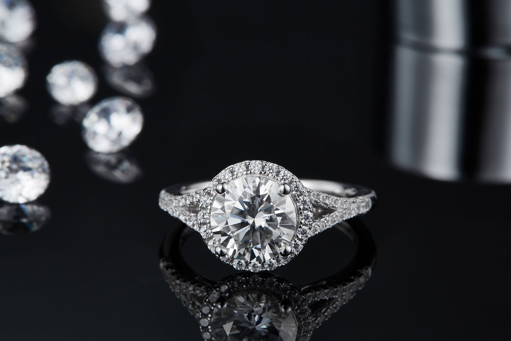 CARISSIE round moissanite halo ring, front view resting on a reflective black surface showing the ring's mirror image