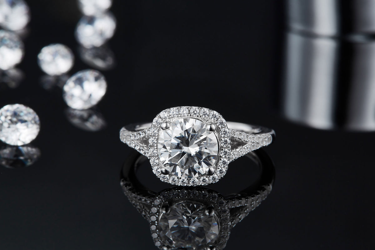 CARISSIE round moissanite halo engagement ring, front perspective on reflective surface emphasizing brilliant center stone sparkle