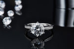 CARISSIE round moissanite solitaire ring, front-facing view resting on reflective black surface showing clear mirror image below.