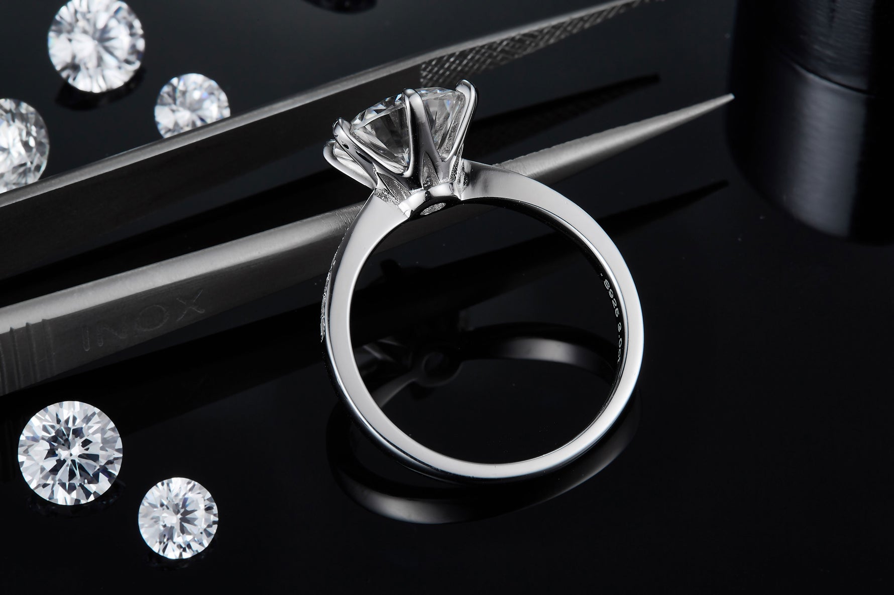 CARISSIE round moissanite solitaire ring, side angle view held by tweezers revealing the interior hallmark and metal thickness.