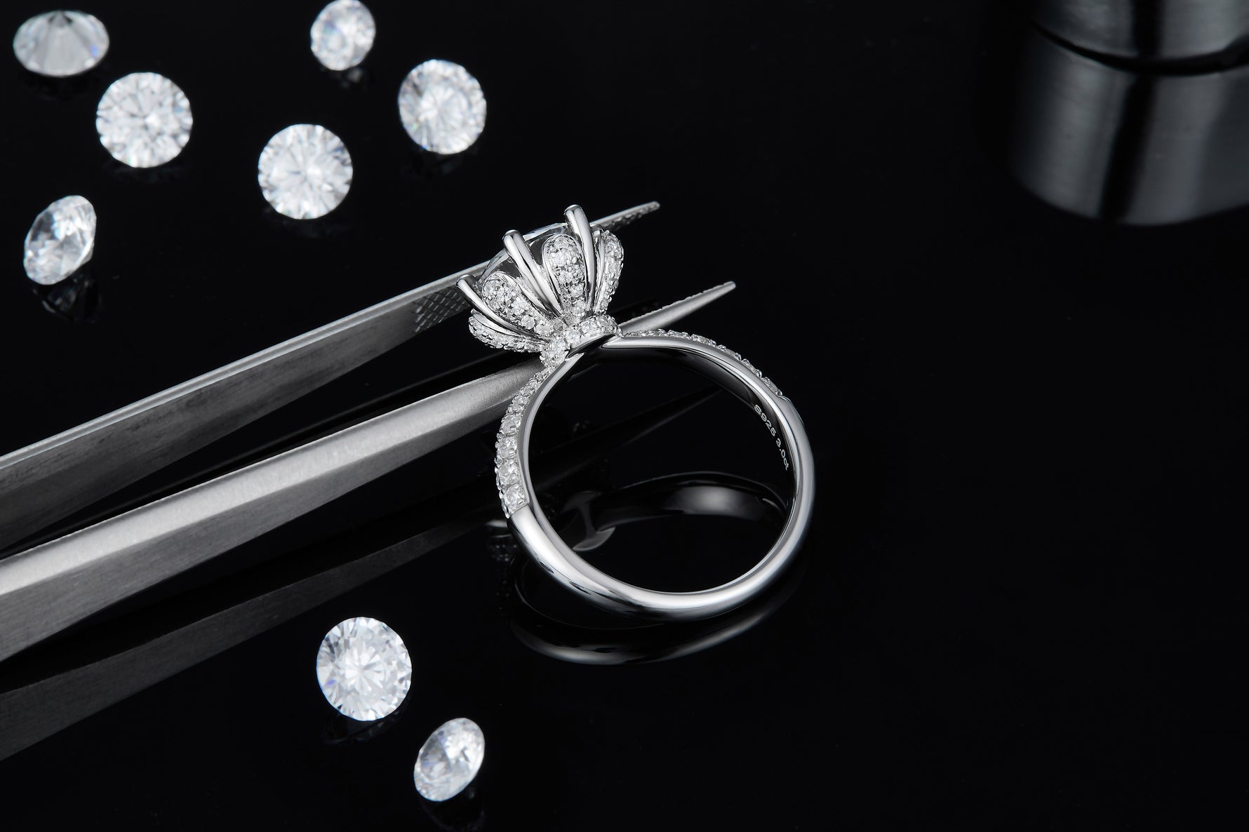 CARISSIE round moissanite engagement ring, held by tweezers to reveal detailed craftsmanship of the pavé gallery
