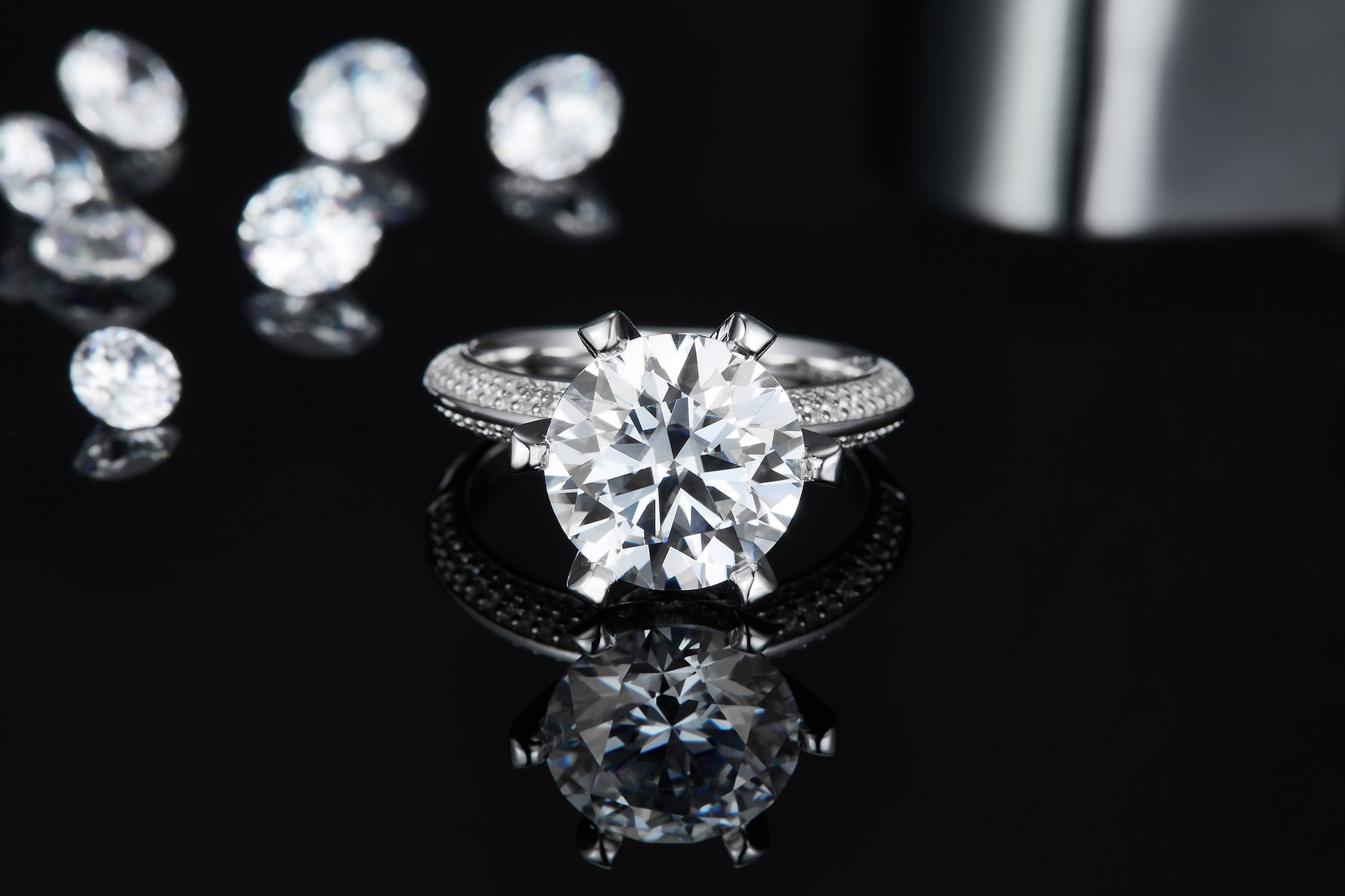 CARISSIE round moissanite ring, lifestyle shot on black reflective surface with loose stones in background