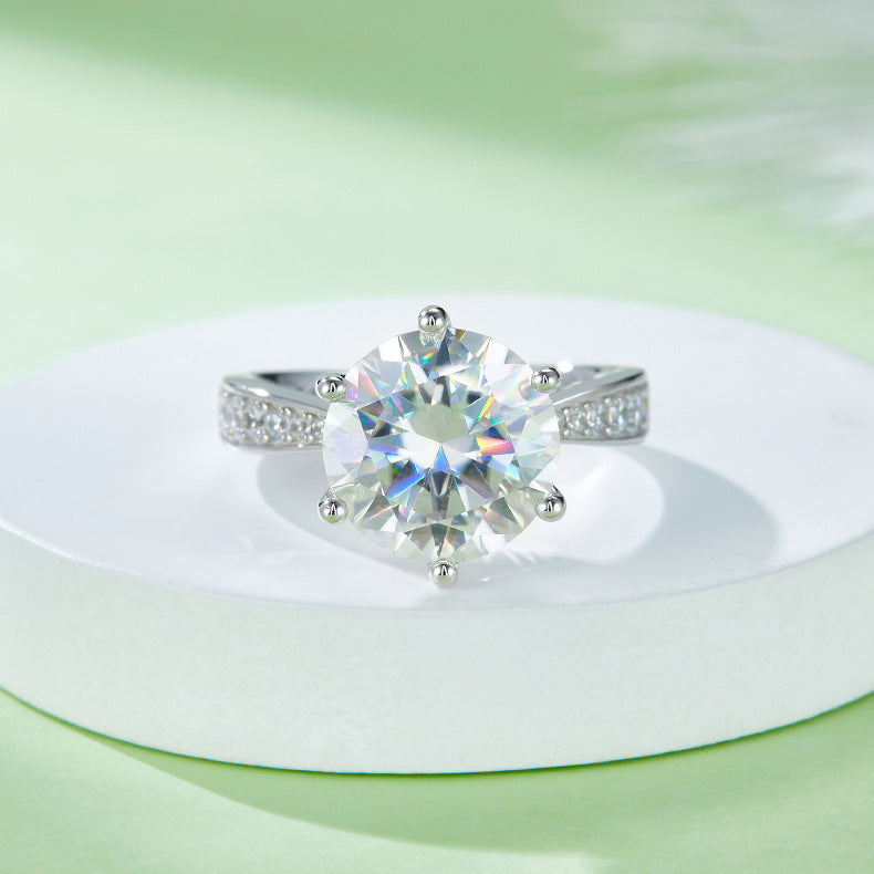 CARISSIE round moissanite engagement ring, styled shot on white display showing rainbow fire within the large center stone