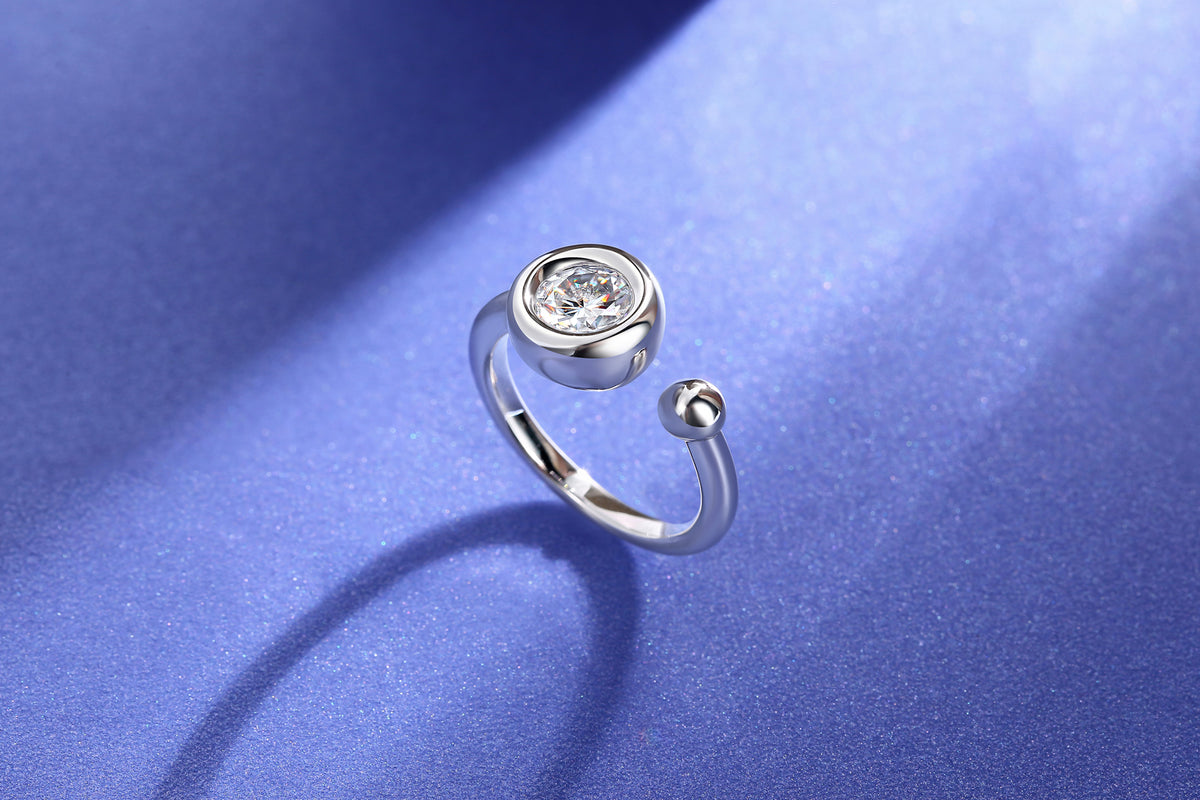 CARISSIE round moissanite bezel ring, standing upright on blue surface revealing curved shank and stone setting