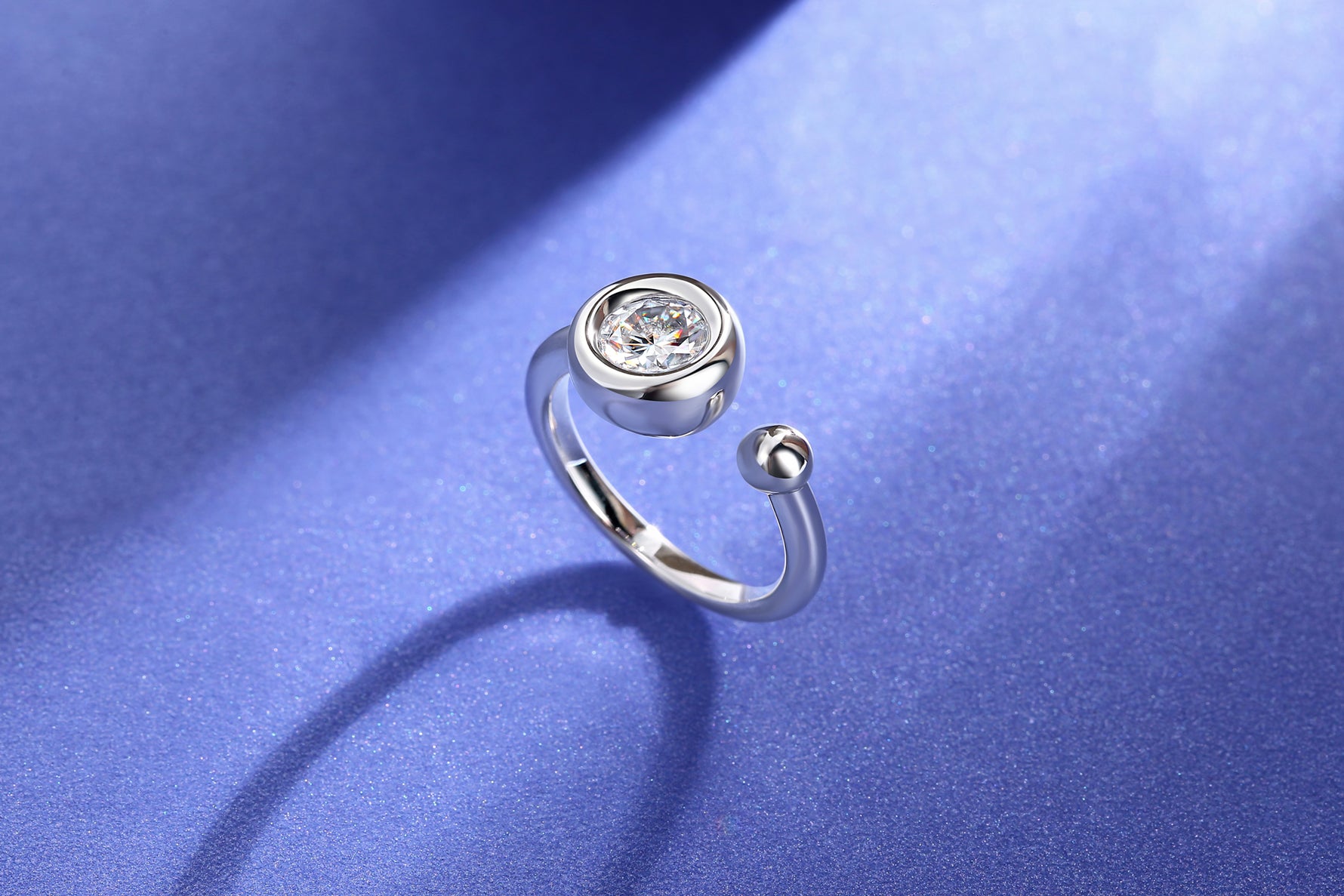 CARISSIE round moissanite bezel ring, standing upright on blue surface revealing curved shank and stone setting