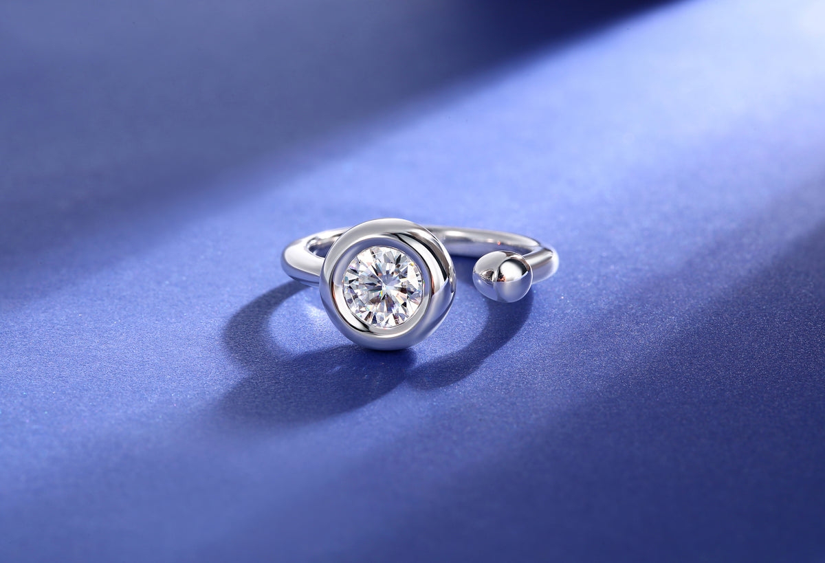 CARISSIE round moissanite bezel ring, side profile on blue background displaying asymmetrical open band shape