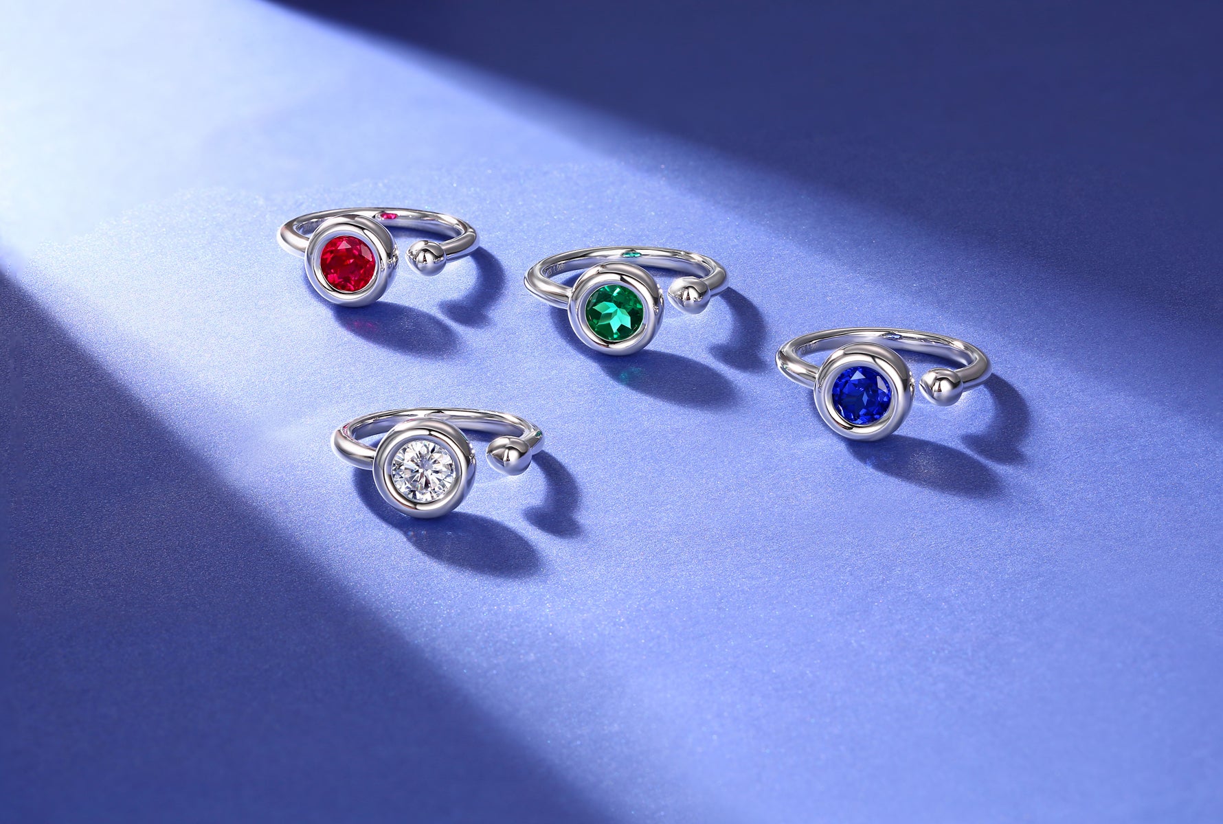 CARISSIE round moissanite bezel rings, flat lay display of four color variations on textured blue surface