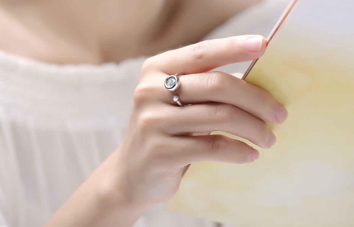 CARISSIE round moissanite bezel ring, white stone option held in hand against soft yellow background