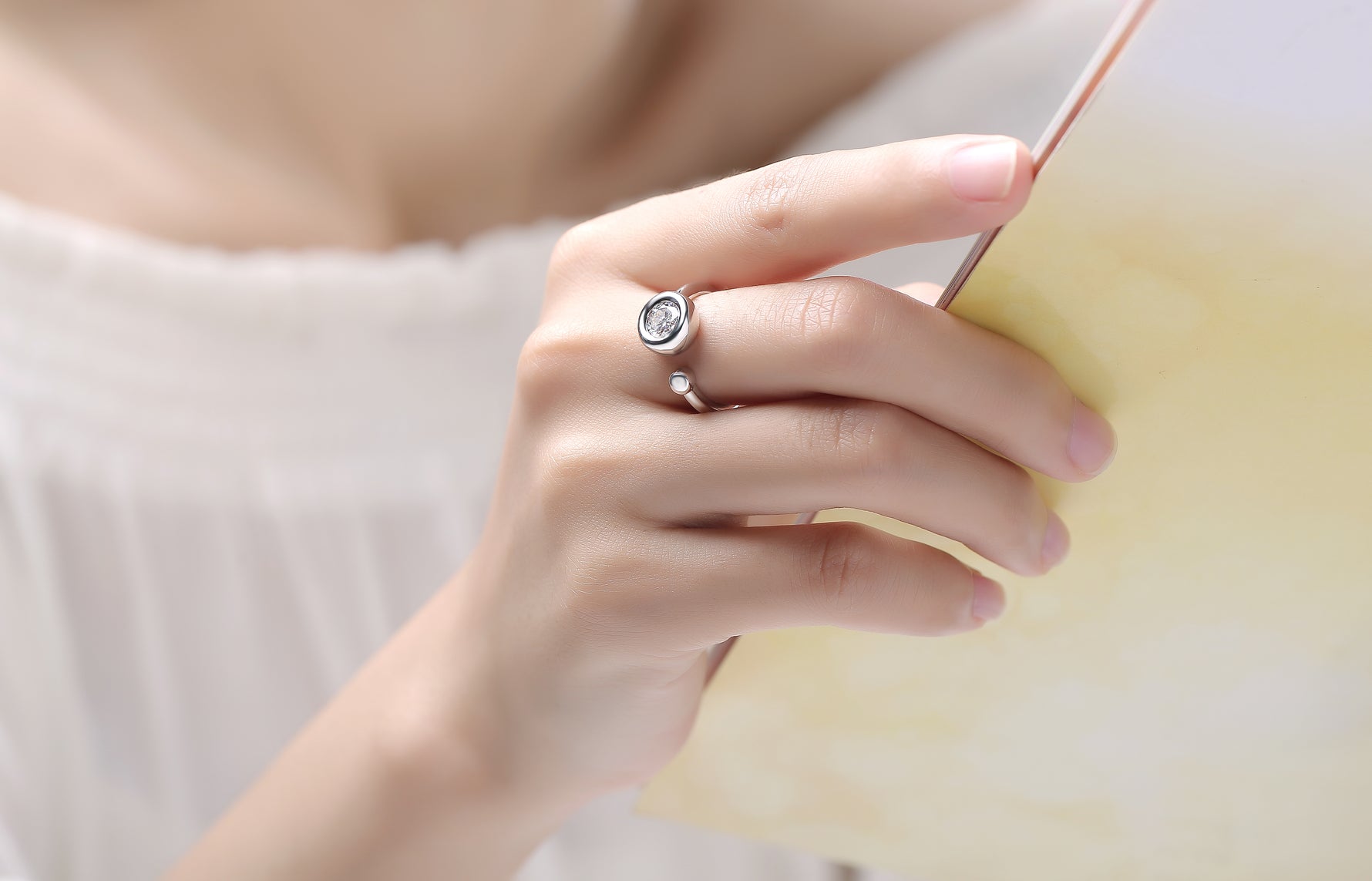 CARISSIE round moissanite bezel ring, white stone option held in hand against soft yellow background