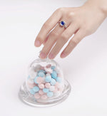 CARISSIE round moissanite bezel ring, blue stone variant shown on hand touching glass candy jar prop