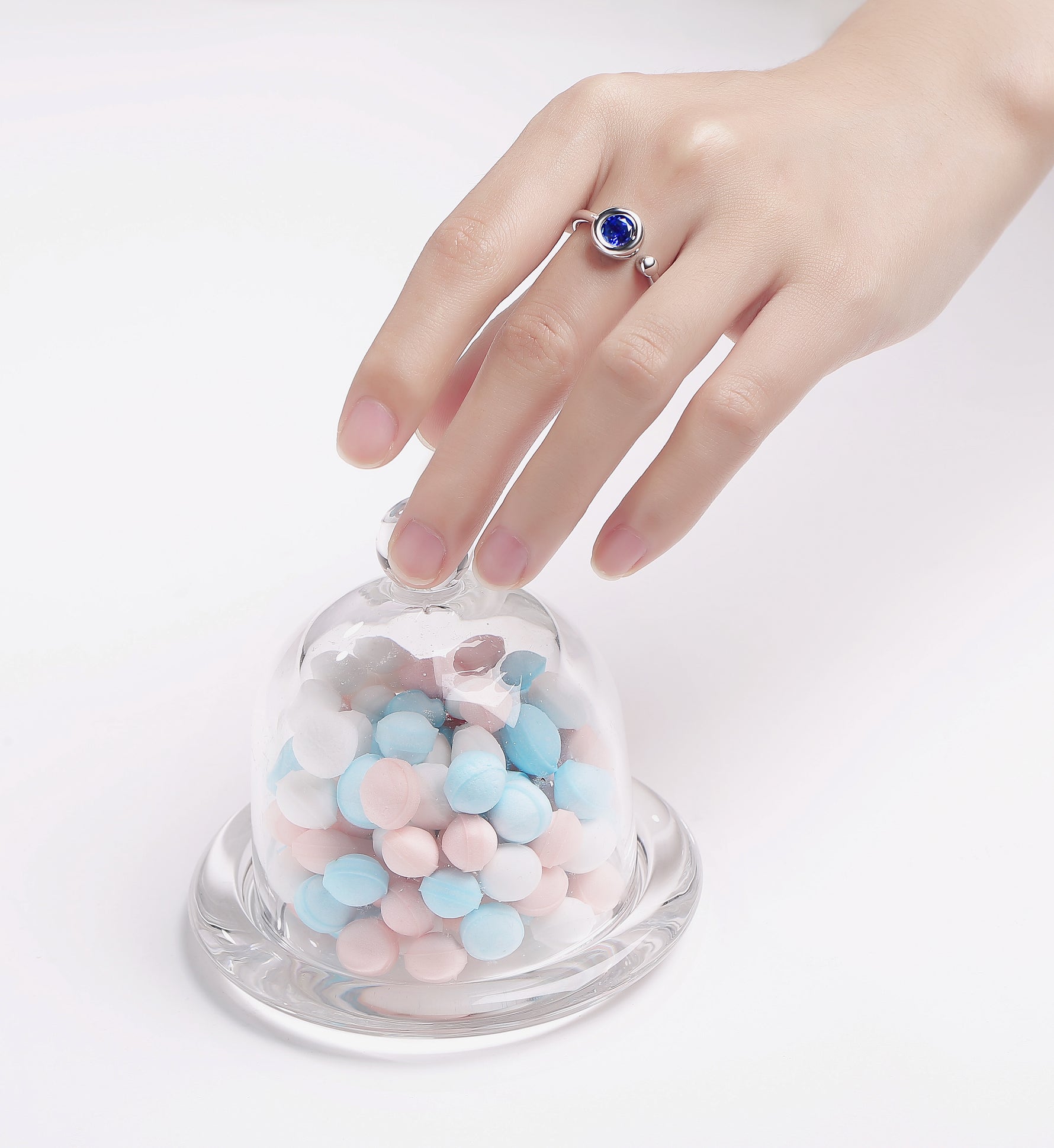 CARISSIE round moissanite bezel ring, blue stone variant shown on hand touching glass candy jar prop