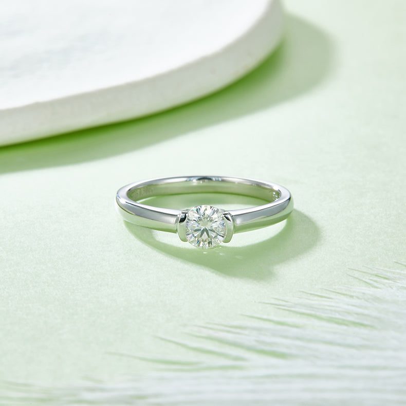 CARISSIE round moissanite solitaire ring, top-down perspective on a pastel surface revealing the circular band shape