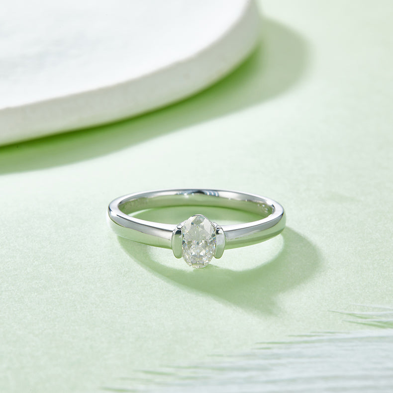 CARISSIE oval moissanite bezel ring, lifestyle shot resting on a textured surface emphasizing the minimalist style