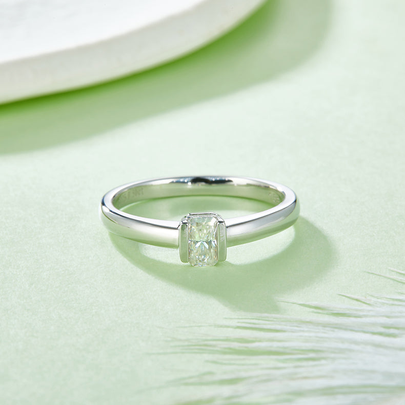 CARISSIE emerald cut bezel engagement ring, top-down perspective on a green surface emphasizing the clean lines of the bezel