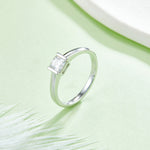 CARISSIE Asscher bezel engagement ring, lifestyle shot on a green background featuring the protective metal rim setting.