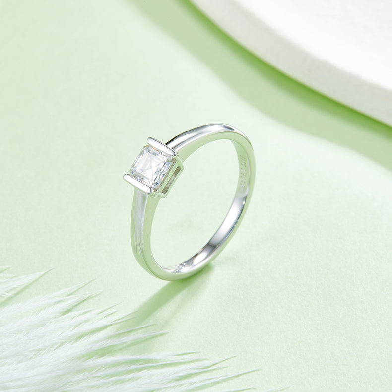 CARISSIE Asscher bezel engagement ring, lifestyle shot on a green background featuring the protective metal rim setting.