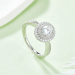 CARISSIE oval moissanite halo engagement ring, lifestyle shot on a soft green background showing sparkle and band curvature