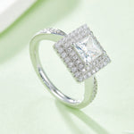 CARISSIE princess halo engagement ring, lifestyle shot on green background displaying diagonal sparkle
