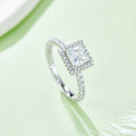 CARISSIE princess halo engagement ring, diagonal angle emphasizing the brilliance of the center stone against a soft green background