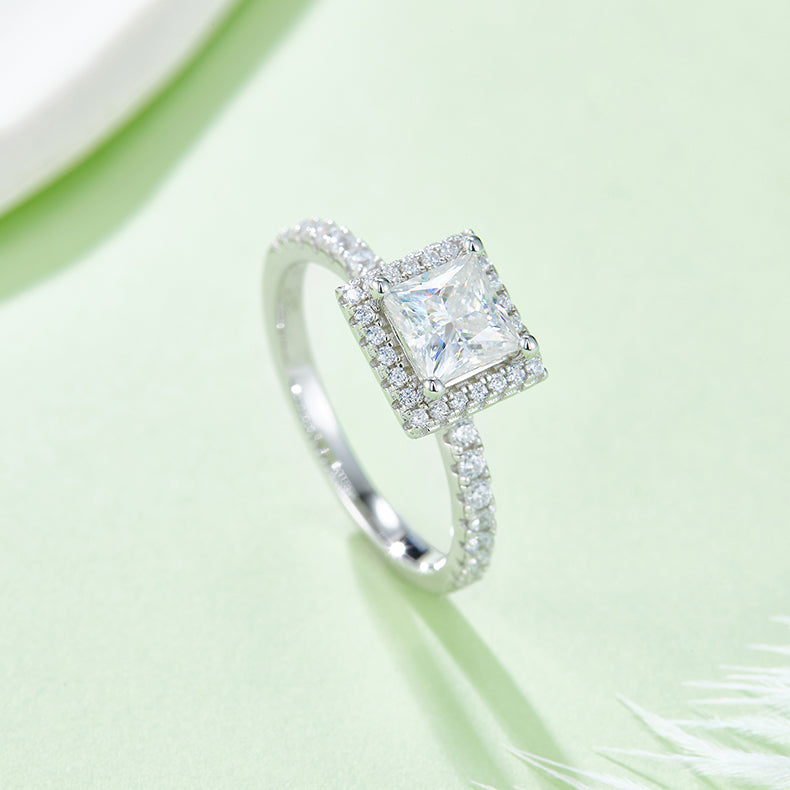 CARISSIE princess halo engagement ring, diagonal angle emphasizing the brilliance of the center stone against a soft green background
