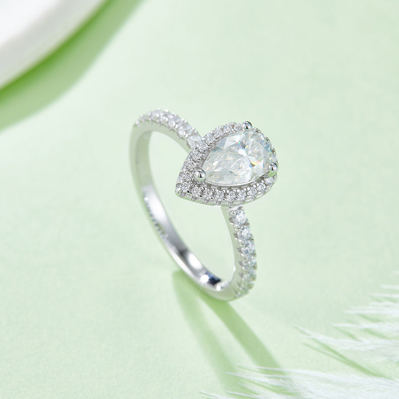 CARISSIE pear moissanite halo engagement ring, lifestyle shot on green background displaying brilliance