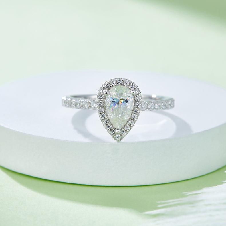 CARISSIE pear moissanite halo engagement ring, close-up on white pedestal showcasing fire in center stone