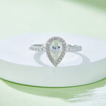 CARISSIE pear moissanite halo engagement ring, close-up on white pedestal showcasing fire in center stone