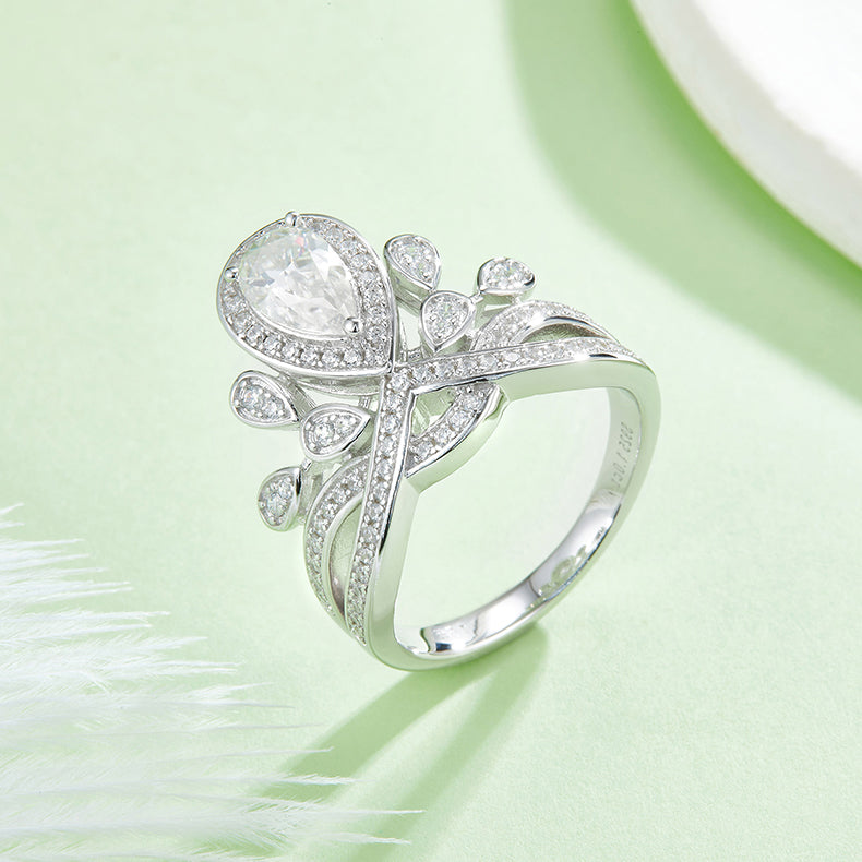 CARISSIE pear moissanite halo ring, lifestyle shot of the white stone version resting on a soft green background