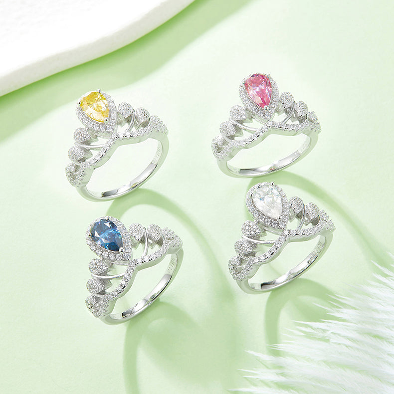 CARISSIE pear moissanite halo ring collection, overhead shot of four colored rings arranged on mint green background with fur texture