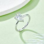 CARISSIE pear moissanite solitaire ring, lifestyle shot on soft green background displaying fire and brilliance in natural light